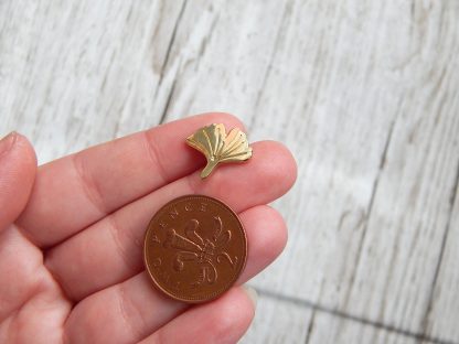 Small ginkgo pin in a hand next to a penny, showing its size of 15mm